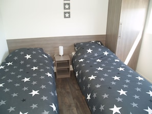 Habitación doble con dos camas, cada una con una colcha estampada con estrellas, una mesita de noche con lámpara y un adorno de estrellas en la pared.