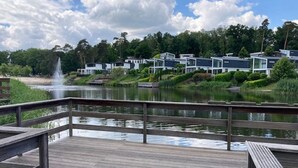 A wooden deck overlooking a lake with a fountain, surrounded by modern buildings with large windows. - Modern Holiday Home Near Brunssummerheide (Brunssum)