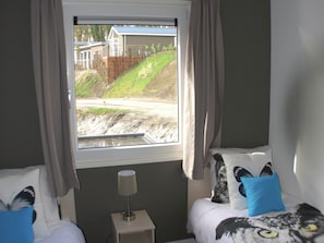 A bedroom with a window view of a construction site, a bedside table with a lamp, and two beds with pillows. - Modern Holiday Home Near Brunssummerheide (Brunssum)