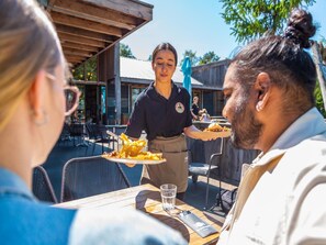 A restaurant with outdoor seating, a waiter serving food, and a casual dining atmosphere. - Cheerful Mobile Home Near Park De Veluwe (Otterlo)