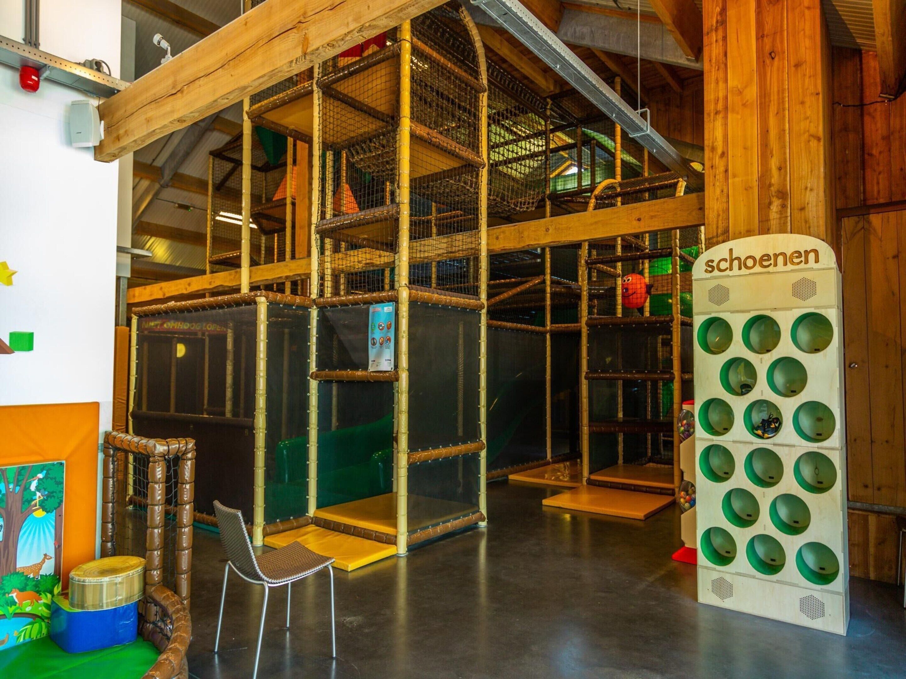 A multi-level indoor play area with wooden structures and netted climbing areas.