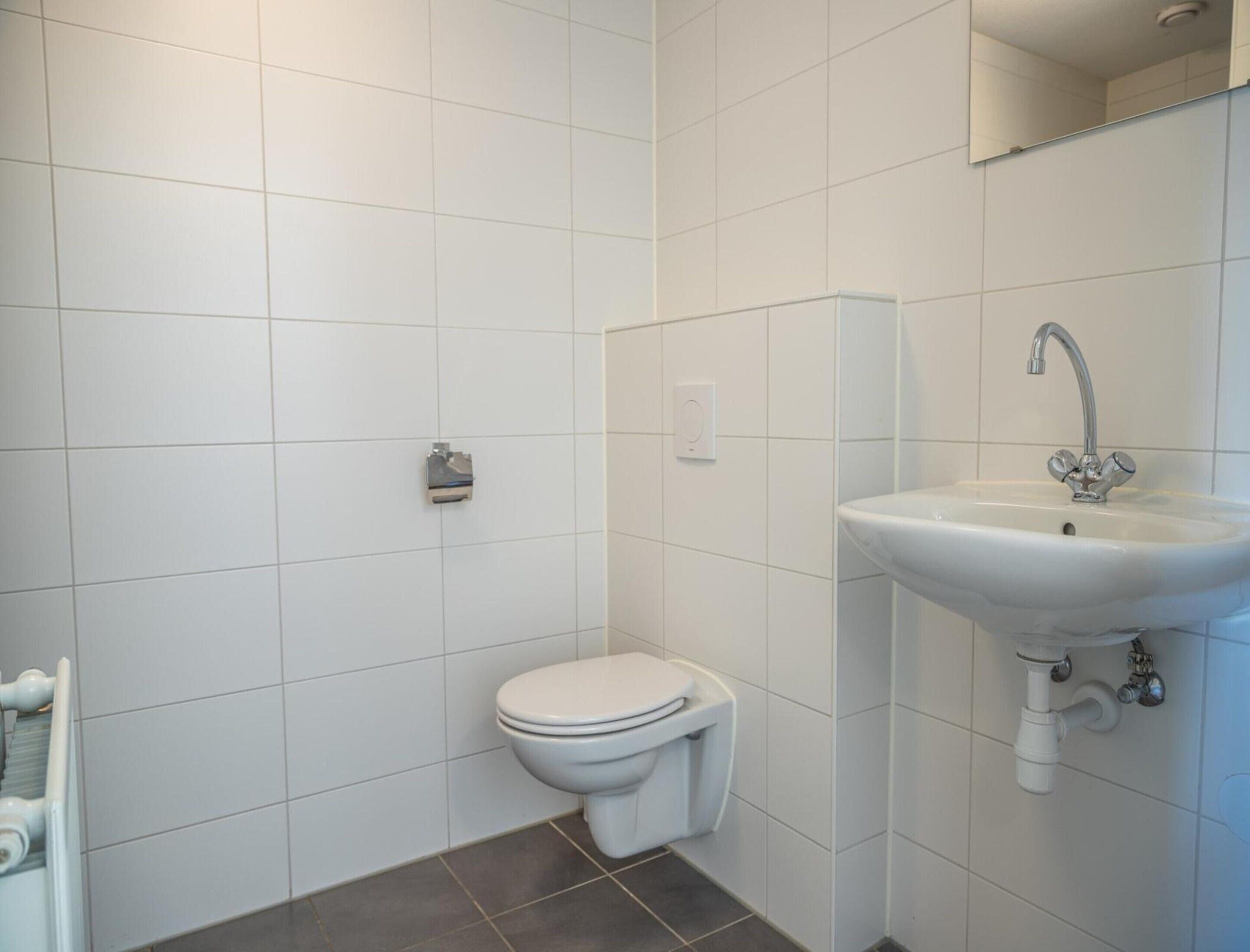A bathroom with white tiles, a toilet, a sink, and a mirror.