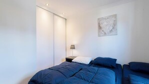 Un dormitorio con cama, mesita de noche, lámpara y un cuadro en la pared.