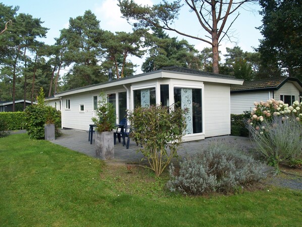 A single-story house with a patio, a small garden, and a view of the surrounding trees.