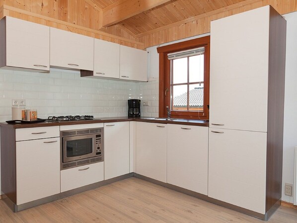 Una cocina moderna con armarios blancos, horno empotrado y ventana con persianas.