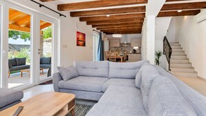 Uma sala de estar moderna com um sofá seccional cinza, vigas de madeira e uma escada que leva a uma cozinha.