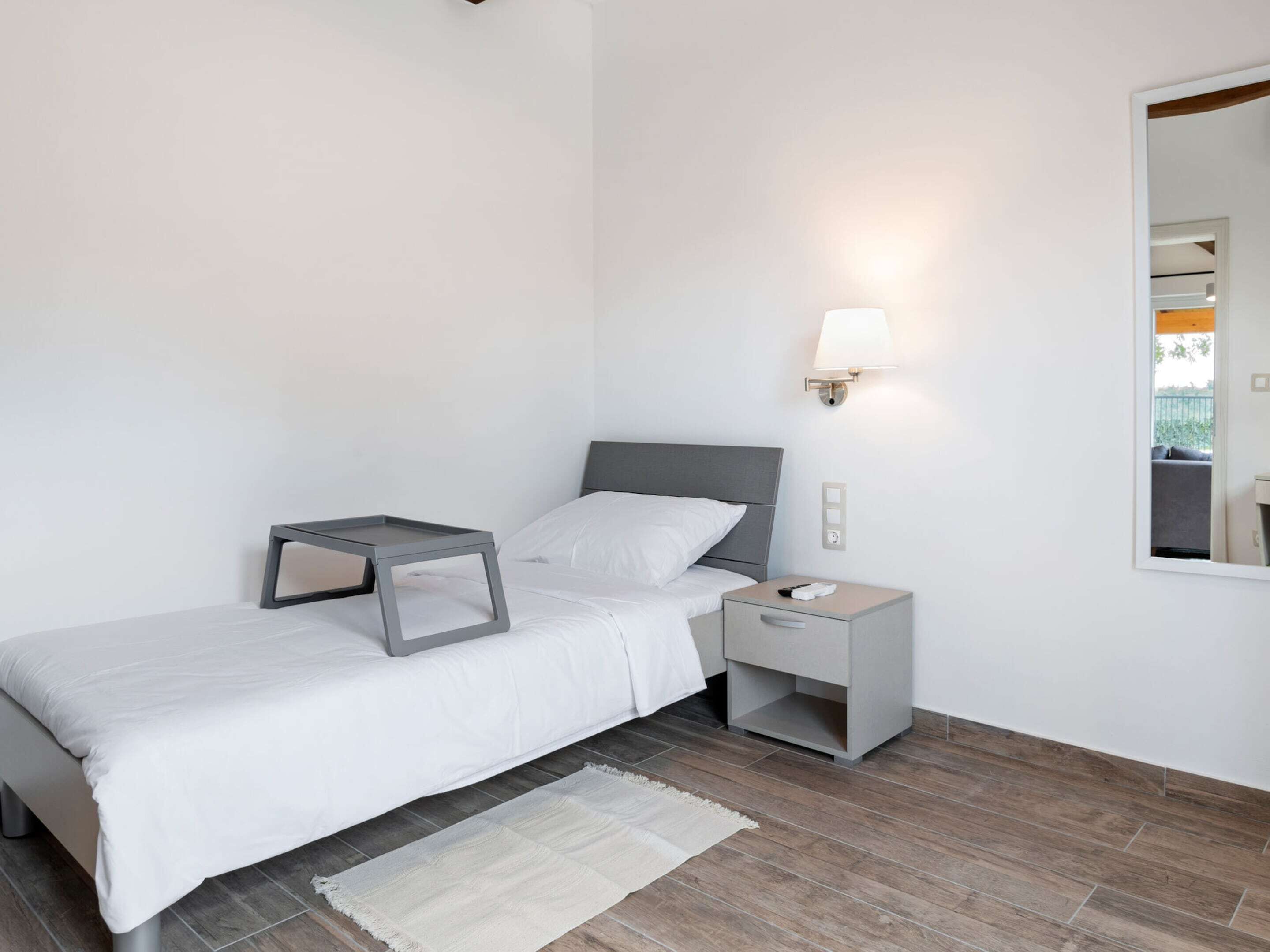 A modern bedroom with a bed, bedside table, nightstand, and a wall-mounted lamp.