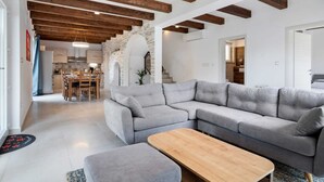 Uma sala de estar moderna com um sofá seccional cinza, uma mesa de centro de madeira e vigas de madeira aparente no teto.