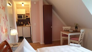 Een slaapkamer met een bed, een bureau met stoel, een kleine kitchenette en een deur naar een andere kamer.