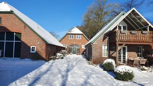 Een sneeuwbedekte oprit die leidt naar een huis van baksteen met een garage en een houten constructie met een balkon.