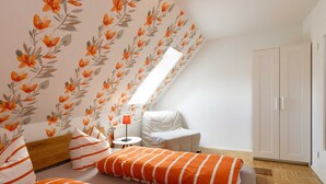 A bedroom with a sloped ceiling, a bed with orange-striped bedding, a bedside table with a lamp, and a wardrobe.