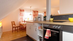 A modern kitchen with a dining area, featuring a wooden dining table, chairs, a coffee maker, and a stove.