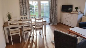 A cozy living room with a dining area, a television, and a view of the outdoors. - Deichhof Dangast, WH Löwenzahn - Holiday apartment Löwenzahn (Varel)