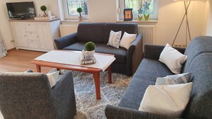 A living room with a grey sofa, a wooden coffee table, and a TV on a cabinet. - Deichhof Dangast, WH Löwenzahn - Holiday apartment Löwenzahn (Varel)