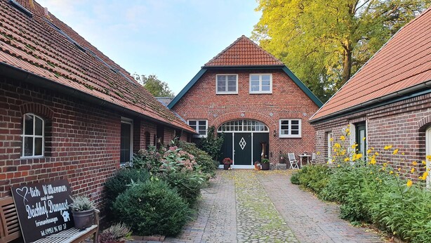 A courtyard with brick buildings, a bench, and potted plants. - Deichhof Dangast, WH Löwenzahn - Holiday apartment Löwenzahn (Varel)