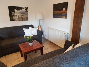 A living room with a sofa, a coffee table with a plant, a lamp, and two paintings on the wall.