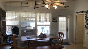 A dining area with a wooden table and chairs, a ceiling fan, and a view of the outside through large windows. - Fish Camp | Old Florida canalfront getaway (Key West)