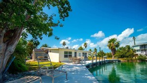 A poolside area with lounge chairs, a small building, and a clear view of the water. - Fish Camp | Old Florida canalfront getaway (Key West)