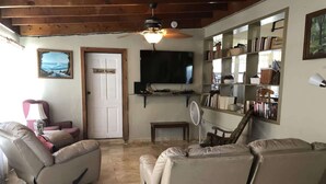 A living room with a sofa, a recliner, a television, a bookshelf, and a ceiling fan. - Fish Camp | Old Florida canalfront getaway (Key West)