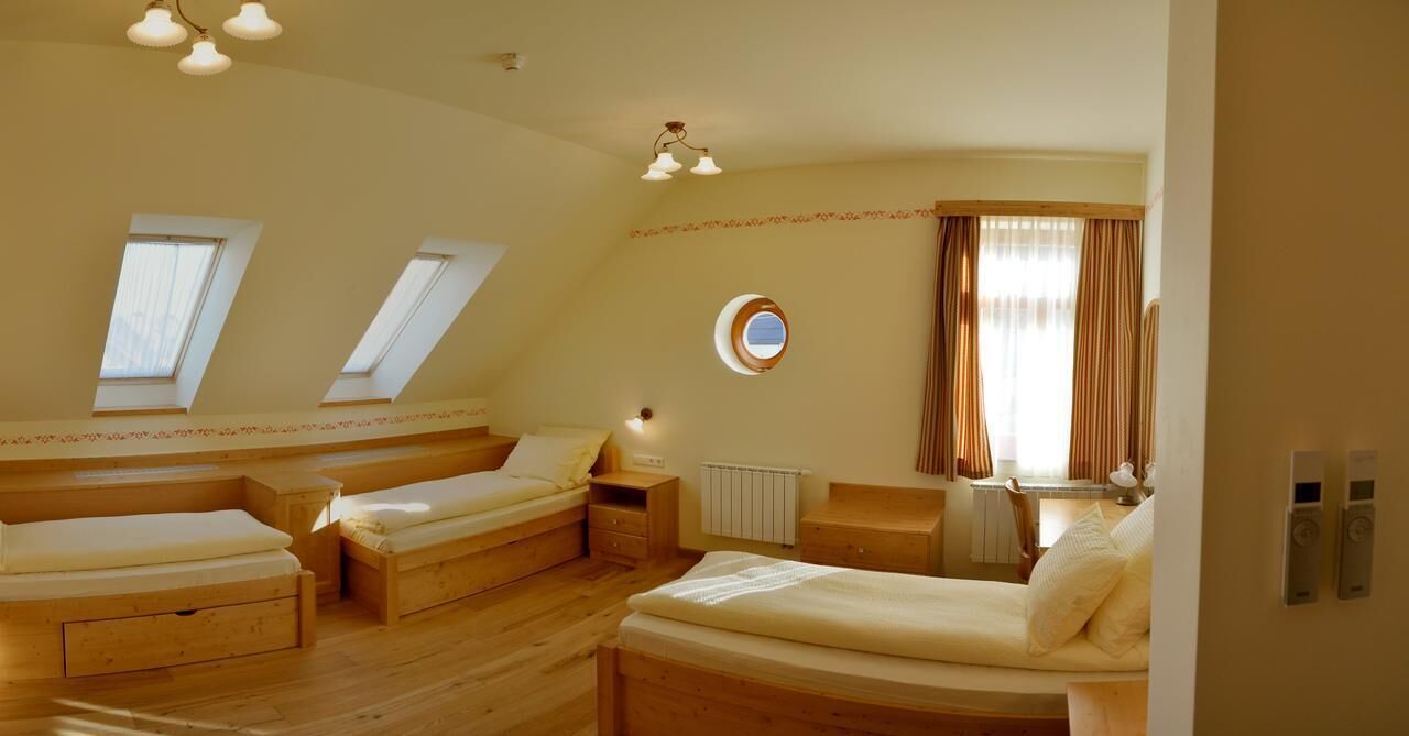 Une pièce avec trois lits en bois, un petit miroir rond, un radiateur et une fenêtre avec des rideaux.