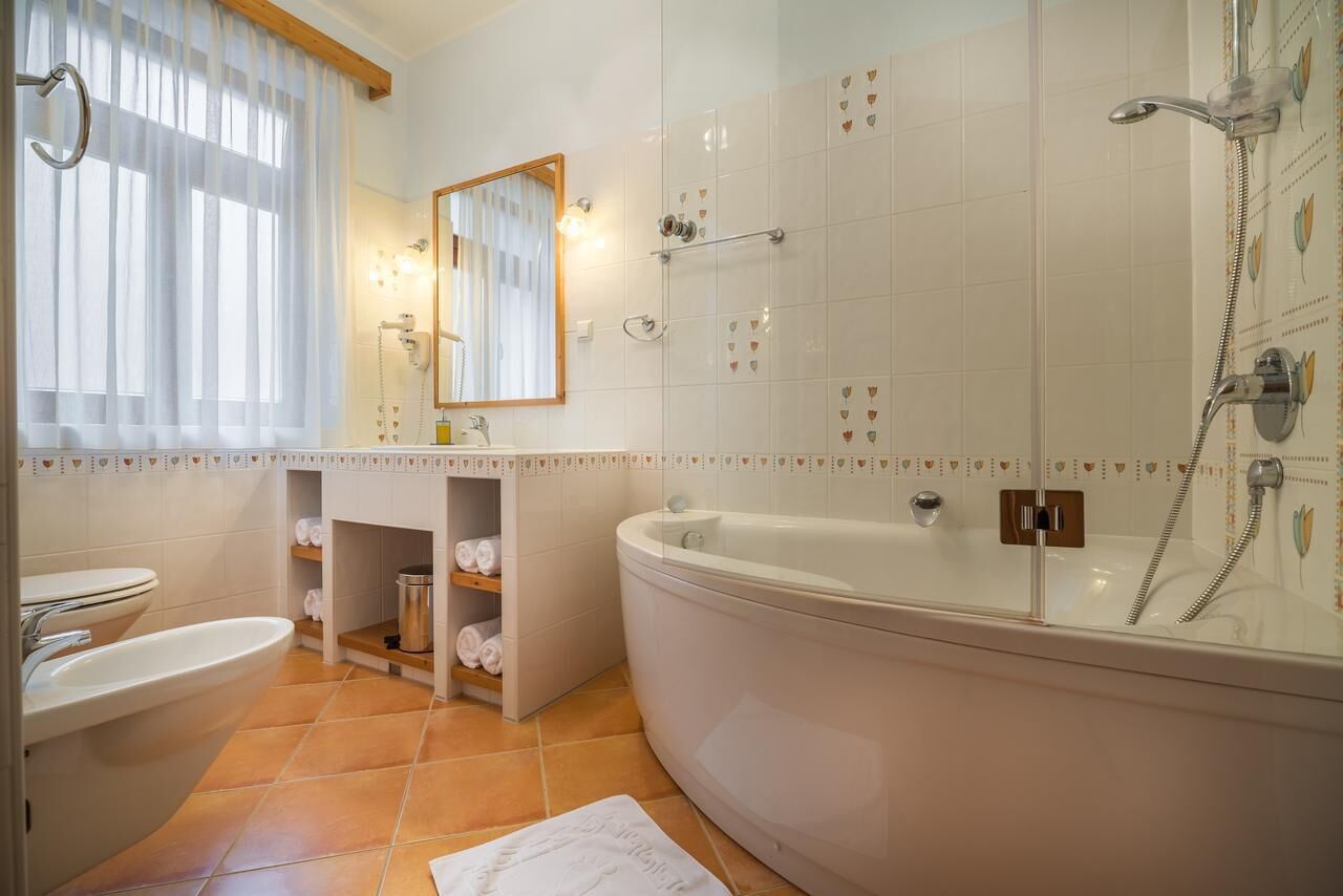 A modern bathroom with a bathtub, a sink, and a toilet. There are shelves with towels and a mirror above the sink.