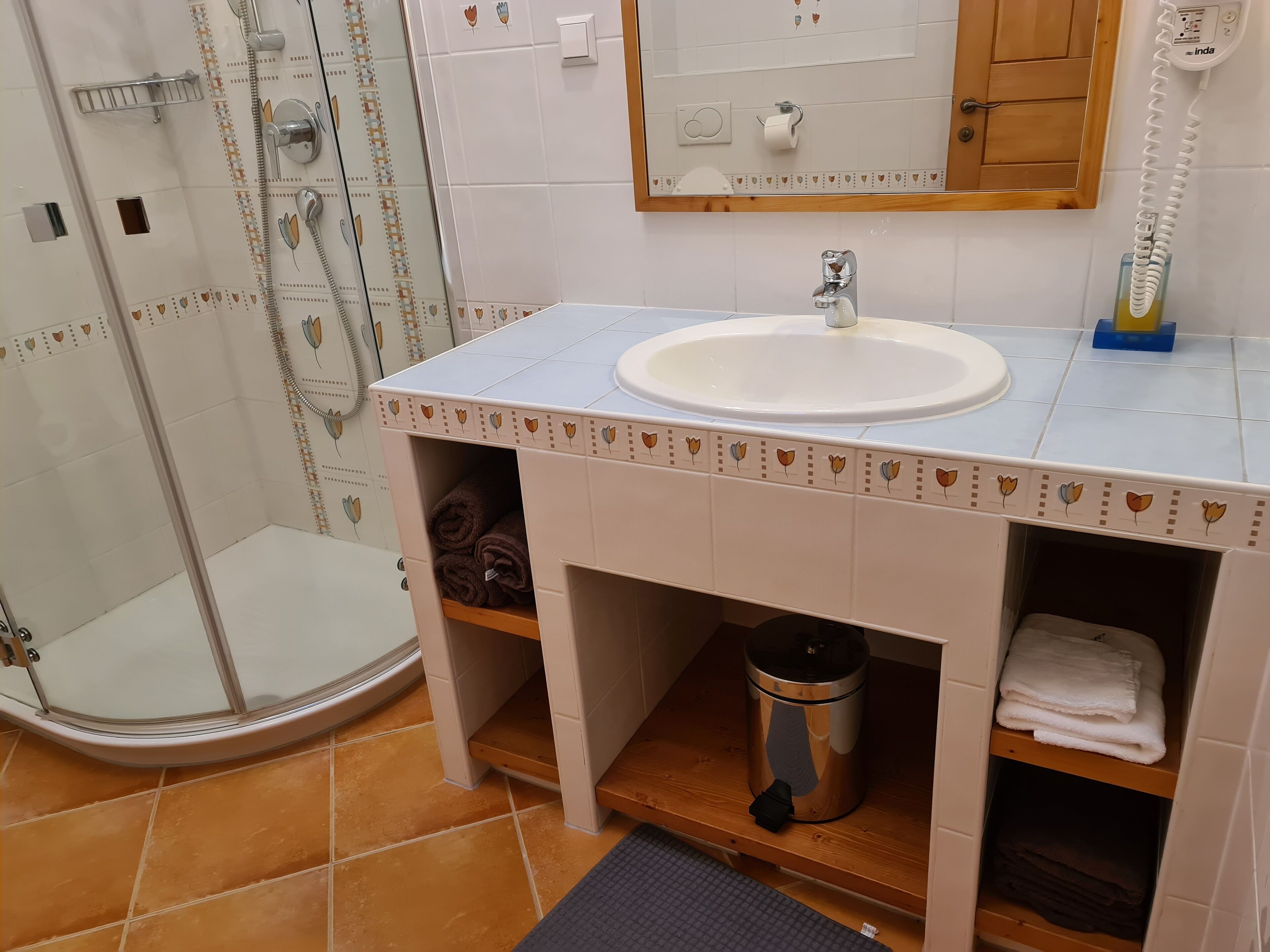 A bathroom with a white sink, a glass shower enclosure, and a wooden shelf with towels.