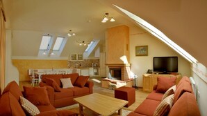 A spacious living area with a fireplace, a television, and a dining area with a kitchen in the background. - Apartments Sitar (Ribnica na Pohorju)