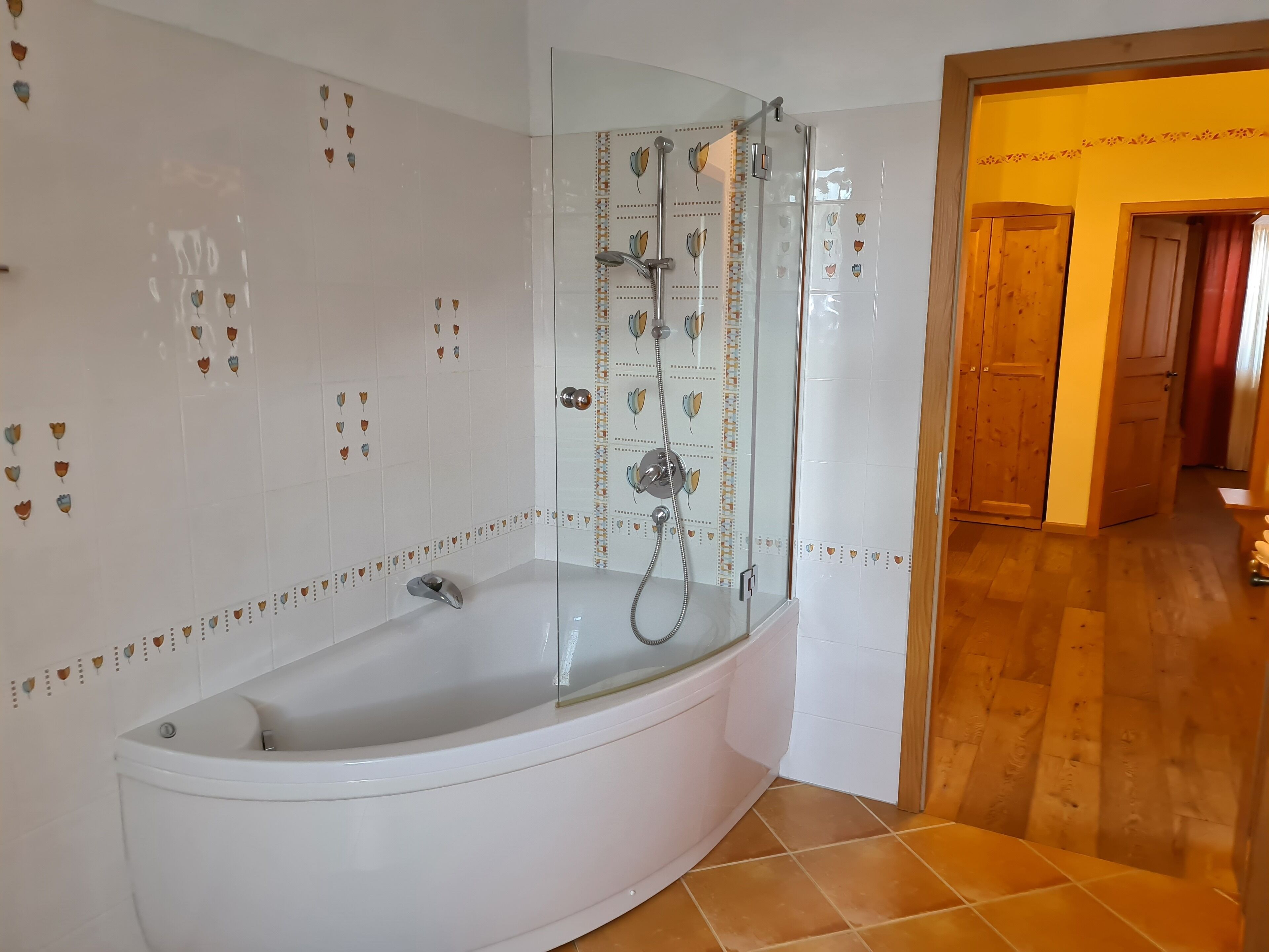 Un bagno con doccia vetro, piastrelle bianche e pavimento in legno.