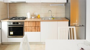 Een moderne keuken met witte kasten, een roestvrijstalen koelkast, een inbouwoven, een gasfornuis en een gootsteen met kraan.