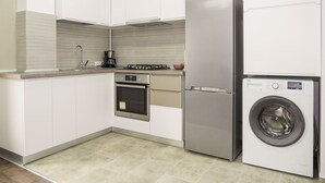 Een moderne keuken met witte kasten, een roestvrijstalen koelkast, een inbouwoven, een koffiezetapparaat en een voorlader wasmachine.