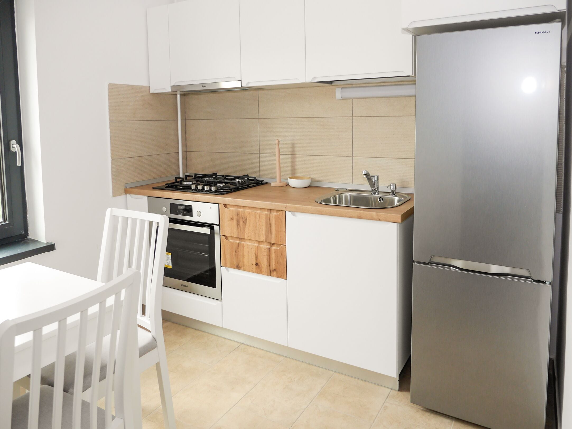 Una cocina compacta con armarios blancos, un refrigerador de acero inoxidable, una estufa a gas y un horno empotrado.