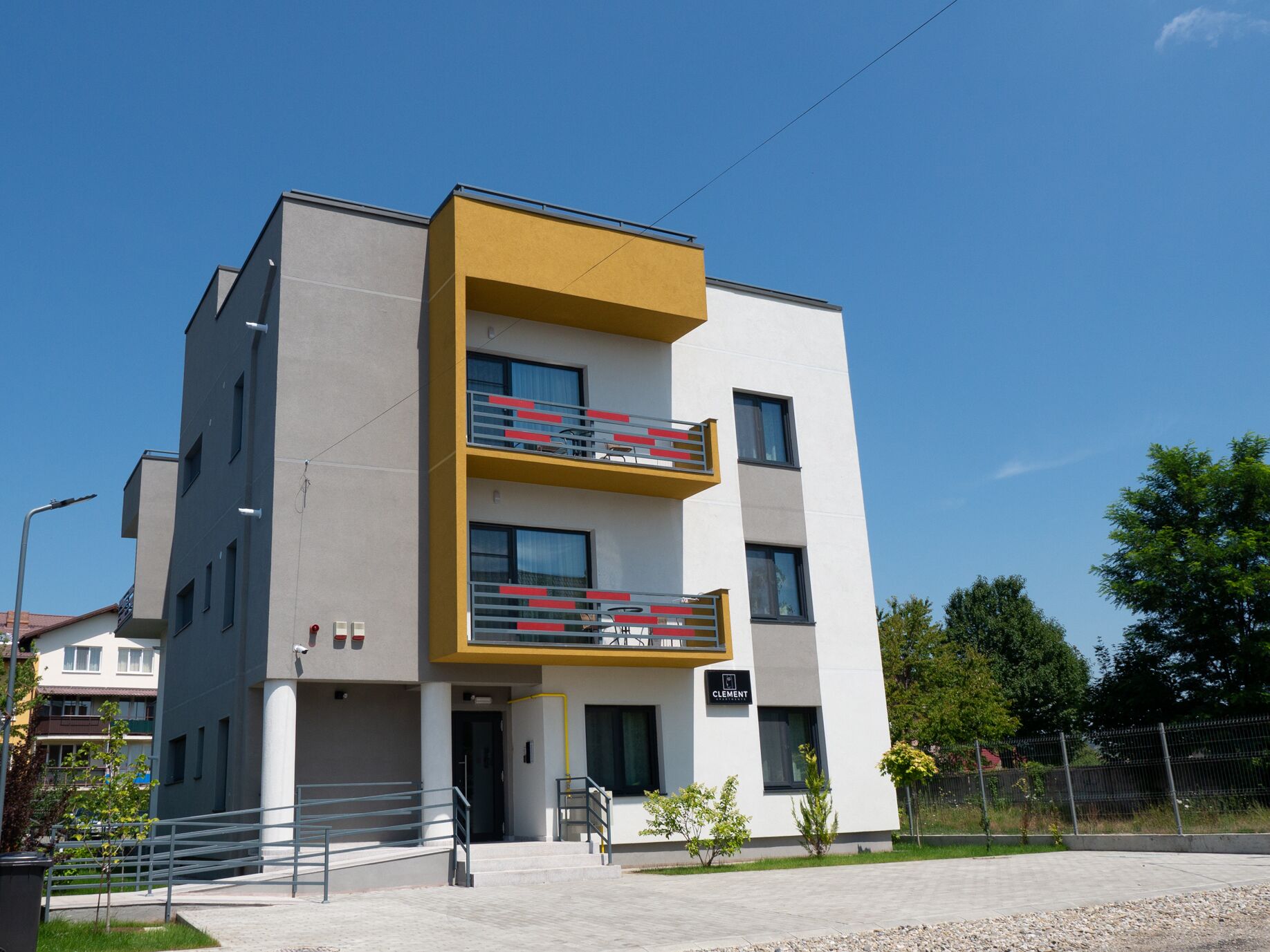 Een modern meerlaags gebouw met een plat dak, een geel accentmuur en een bord waarop staat dat het een 'Clement' eigendom is.