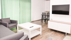 Een moderne woonkamer met een grijze bank, een witte salontafel en een televisie op een witte kast.
