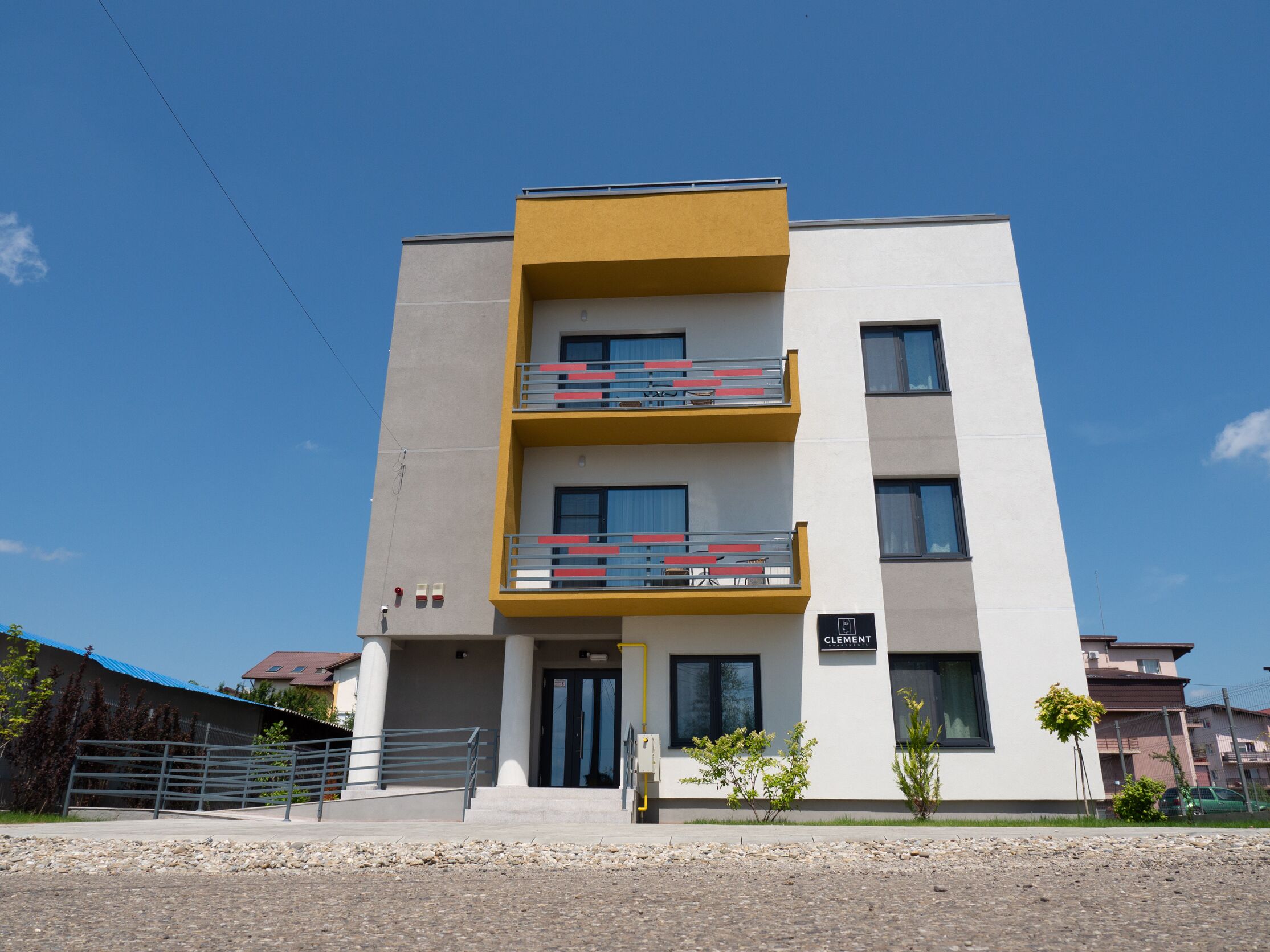 Un edificio moderno de varios pisos con techo plano, una pared de acento amarilla y balcones con barandillas rojas.