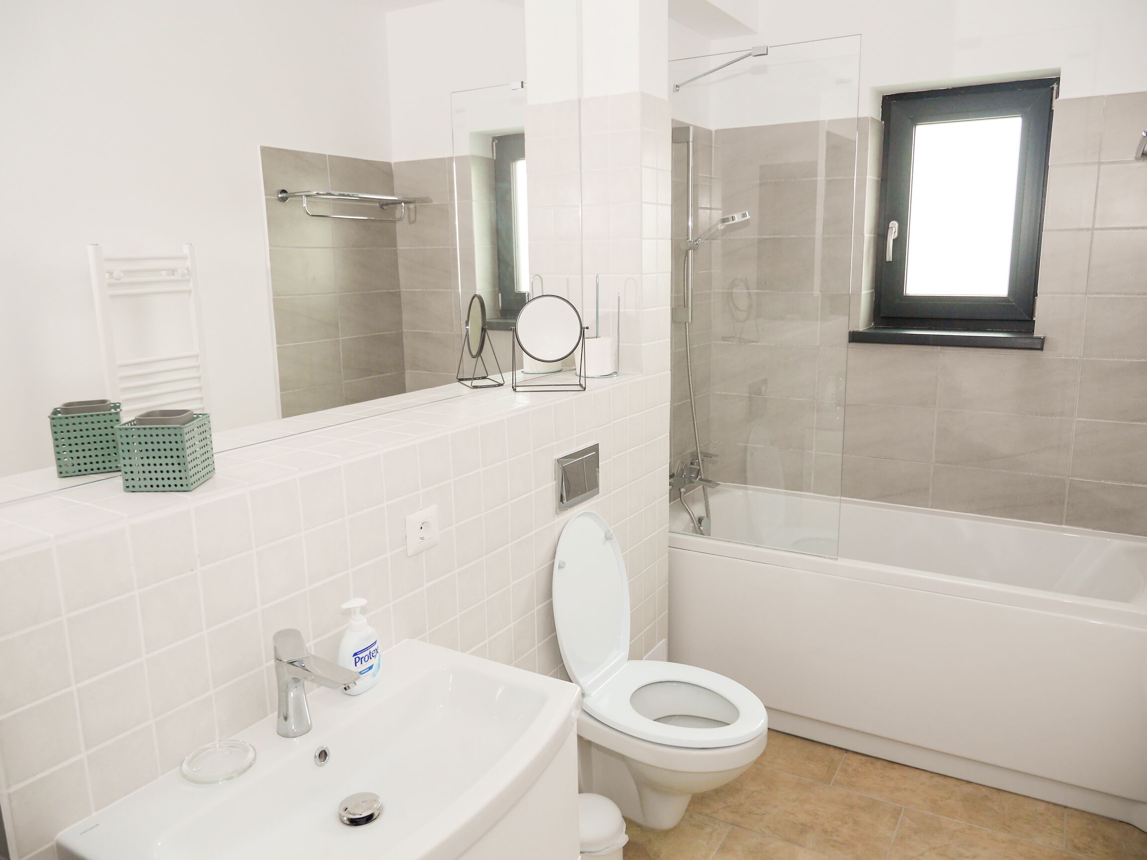 A bathroom with a white sink, toilet, and shower. There are two green baskets on the sink counter.