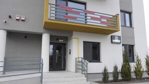 Een modern gebouw met een geel balkon, een zwarte deur en een bord met de tekst 'Clement Apartments'.
