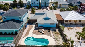 Un barrio residencial con una casa grande azul, una piscina y vista al océano.