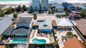 Un área residencial costera con una amplia casa de dos plantas, una piscina y una playa al fondo.