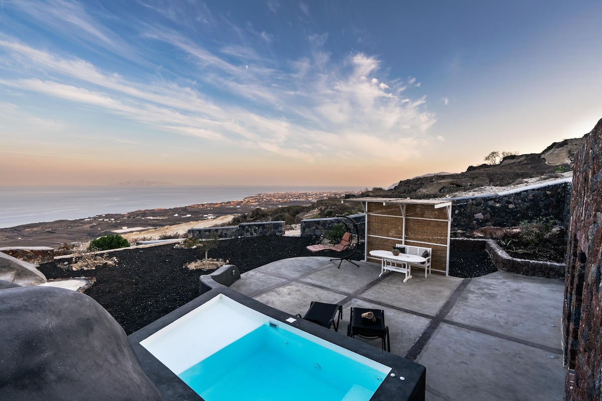 A rooftop pool with a view of the sea, outdoor seating, and a stone wall.