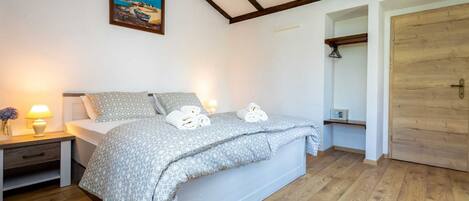 A bedroom with a bed, bedside tables, a painting, and a wooden door.