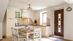 Une cuisine avec un coin repas, des meubles blancs, un pare-feu en carrelage et une table à manger en bois avec des chaises.