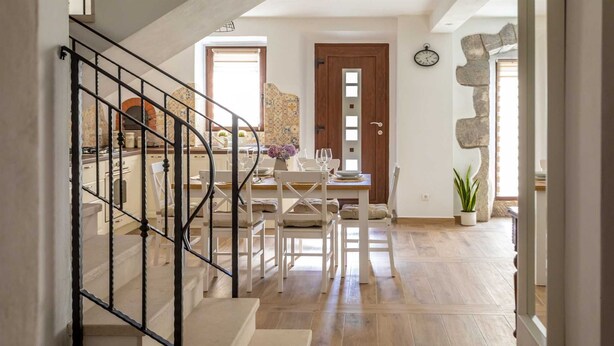 Un escalier mène à un espace repas où se trouve une table en bois dressée pour un repas, une plante en pot et un mur en pierre qui sert d’élément décoratif.