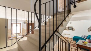 Un vaste espace de vie agrémenté d’un escalier en courbe, d’un canapé bleu et d’une table à manger sur laquelle sont disposés des fruits.