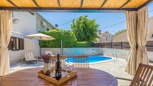 Un espace extérieur abrité, doté d’une piscine, de mobilier en bois et d’une table mise avec une bouteille et des verres.