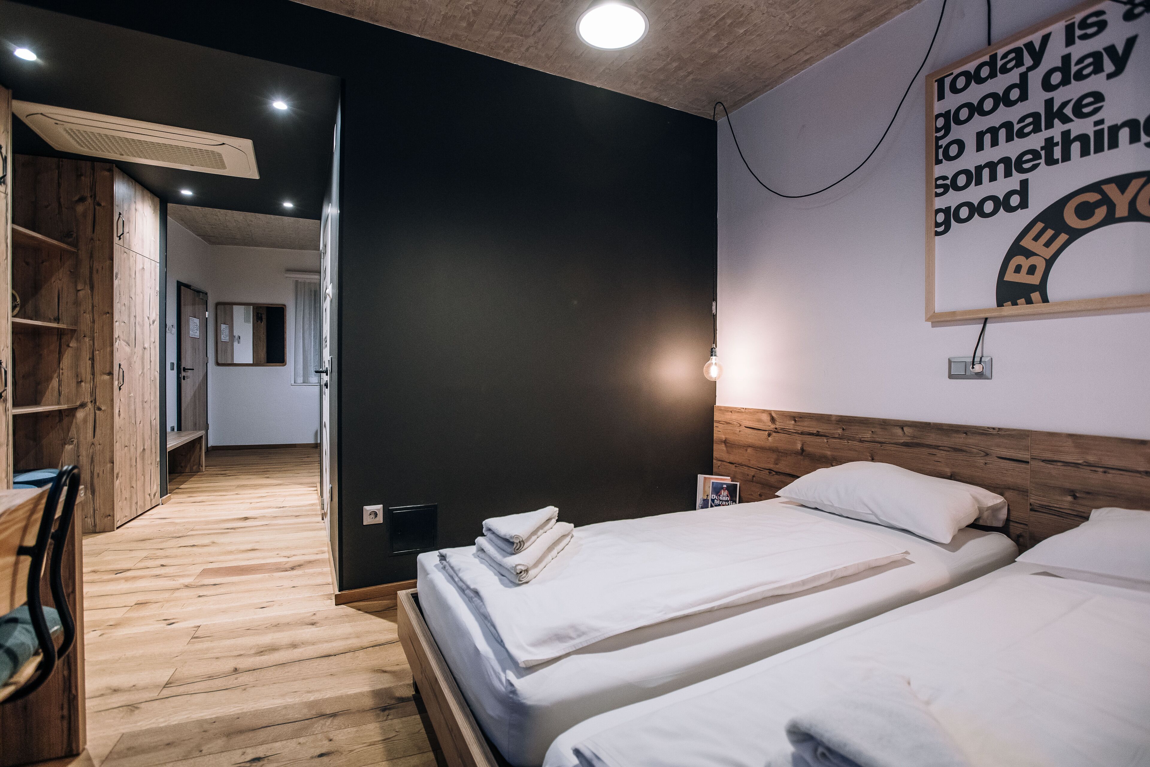 A modern hotel room with two beds, wooden flooring, a large mirror, and a motivational quote on the wall.