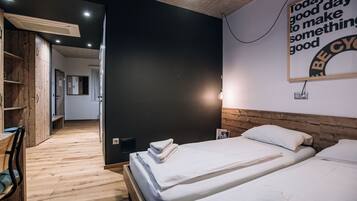 A modern hotel room with two beds, wooden flooring, a large mirror, and a motivational quote on the wall.