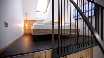 Un dormitorio moderno con cama alta, tragaluz y barandilla negra.