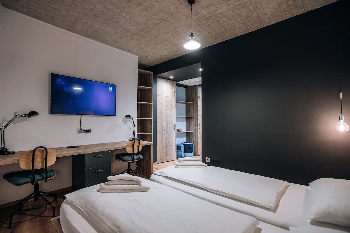 Une chambre moderne équipée d’une télévision, d’un bureau, de deux lits et d’une armoire.