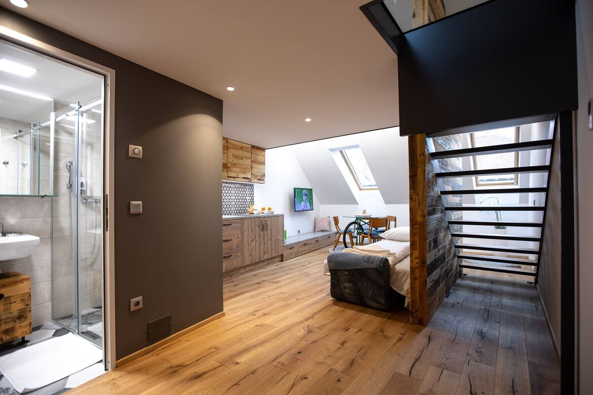 Une chambre de style loft moderne, dotée d’une lucarne, d’un plancher en bois, d’un banc intégré et d’une salle de bain ouverte avec une douche à parois de verre.
