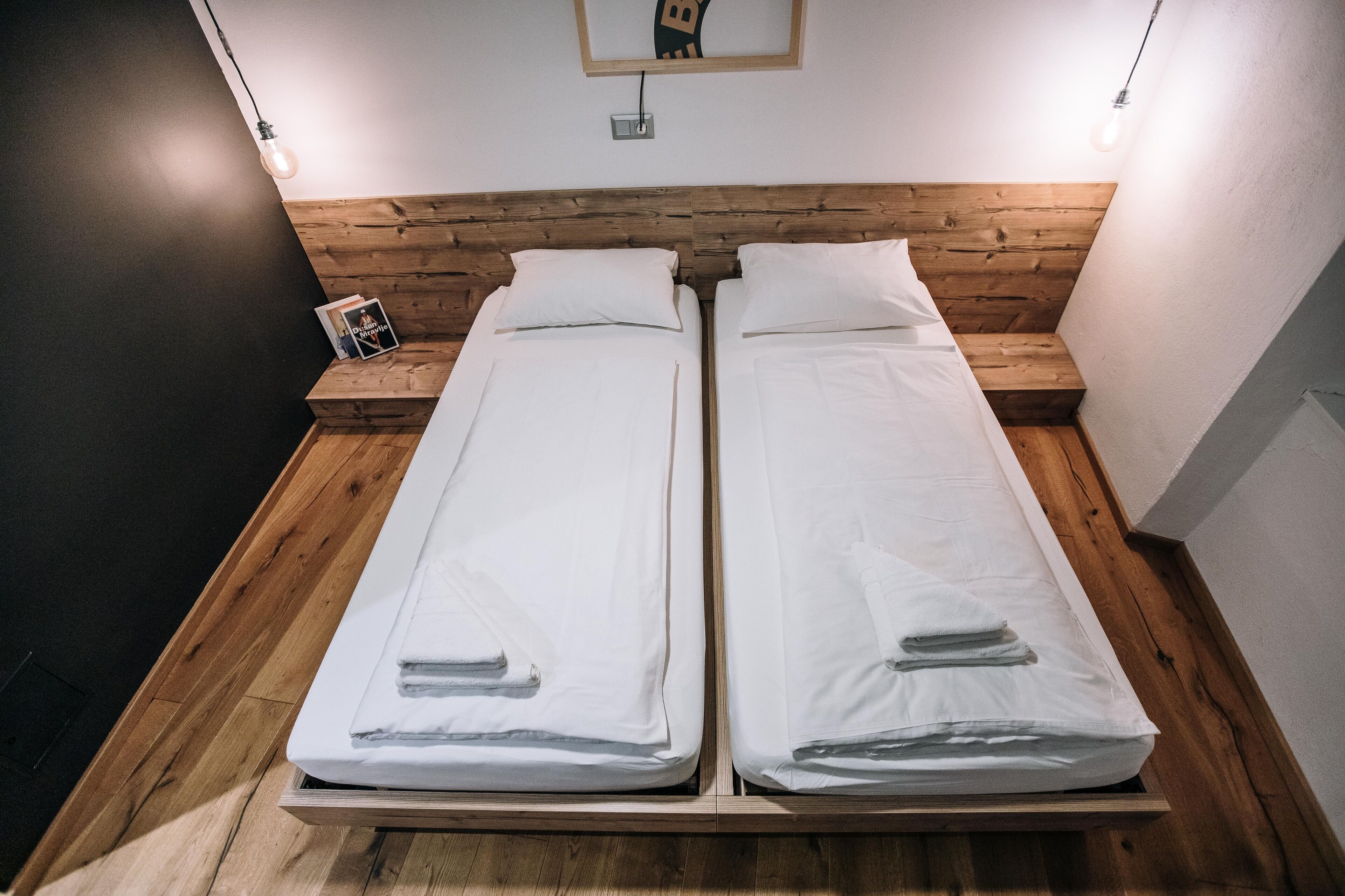 A double bed with wooden headboard and white linens, two bedside tables, and a framed picture on the left side.